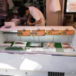 Street market in Japan selling fresh fish, man preparing food. Explore local cuisine on a Japan tour.