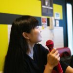Woman enjoying karaoke in Japan, holding a red microphone in a lively room, highlighting unique tour experiences.