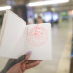 Hand holding a stamped travel notebook in a Japanese train station, perfect for Japan tour adventures.