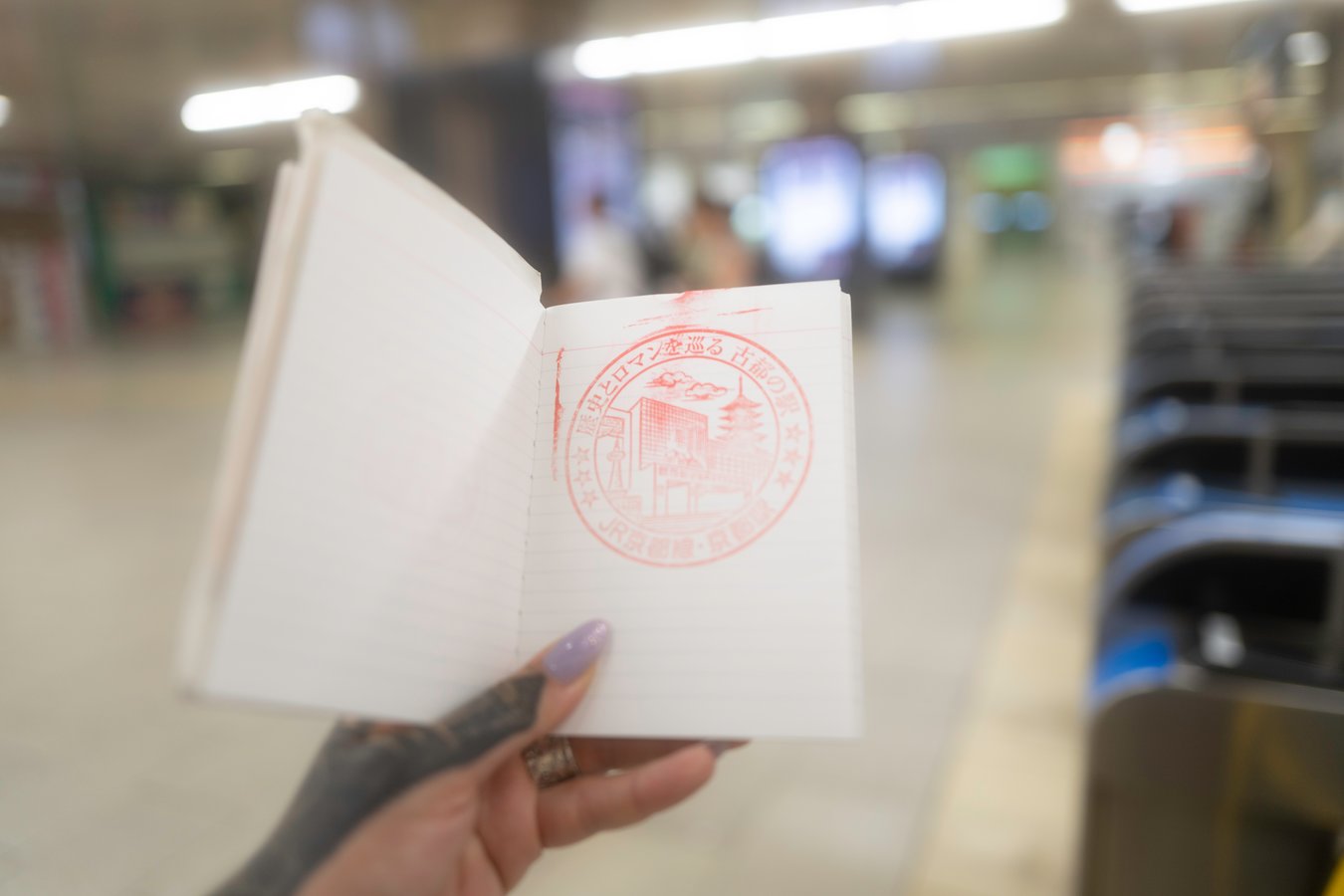 Hand holding a stamped travel notebook in a Japanese train station, perfect for Japan tour adventures.