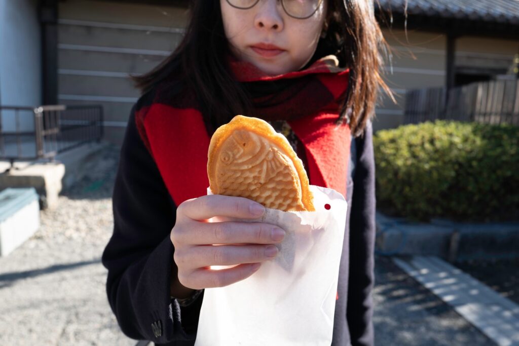 Person enjoying taiyaki, a fish-shaped Japanese snack, during a cultural tour in Japan.