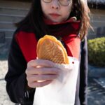 Person enjoying taiyaki, a fish-shaped Japanese snack, during a cultural tour in Japan.