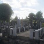 Japanese cemetery with stone monuments and lush trees under a sunny sky, reflecting cultural heritage.